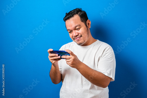 Funny Fat Asian Guy Playing Games on Tablet Smart Phone against blue background