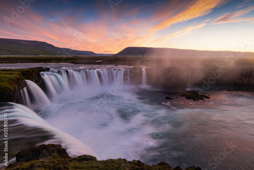 Big blue stream of Godafoss Waterfall and colourful of sky cover  lava rock cliff in twilight  Summer  Iceland.