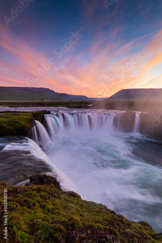 Big blue stream of Godafoss Waterfall and colourful of sky cover  lava rock cliff in twilight  Summer  Iceland.