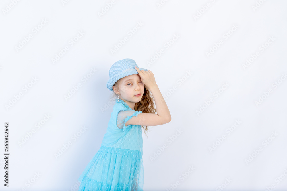 a beautiful 6-year-old girl in a blue dress holds a hat on a white isolated background, space for text