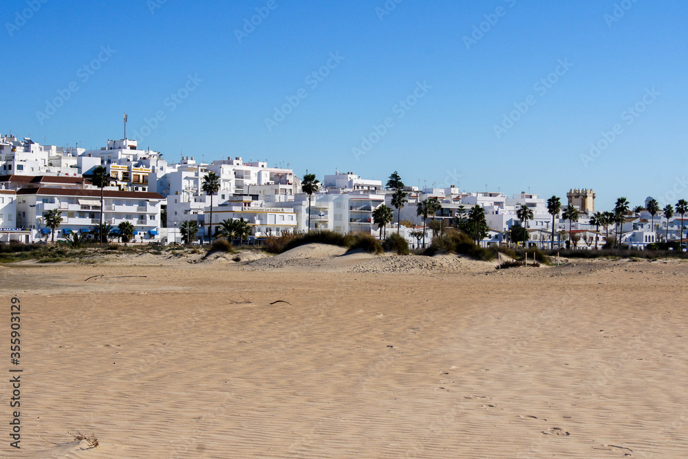 Conil de la Frontera / Spain - December 31, 2016 - Panoramic view from the beach side of the village of Conil at Costa de la Luz, Spain (Andalucia) under a blue sky. Light sandstorm at the beach.