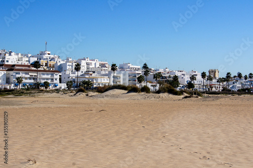 Conil de la Frontera / Spain - December 31, 2016 - Panoramic view from the beach side of the village of Conil at Costa de la Luz, Spain (Andalucia) under a blue sky. Light sandstorm at the beach. © ThePhotoFab