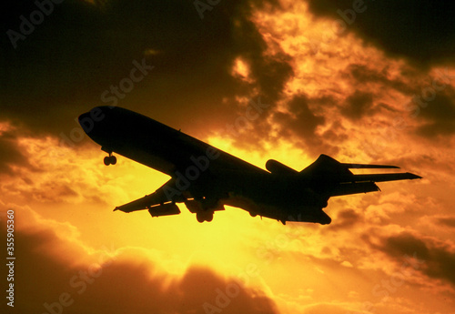 Boeing 727 jet airliner on landing approach silhouetted against setting sun