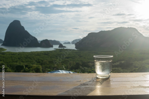 water glass on wood table in the morning sunrise of Samet Nang She is the best and famous view point on Phang nga bay in Southern Thailand.