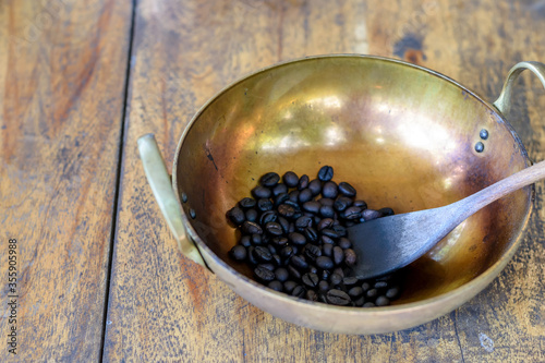Roasted coffee beans in a brass pan on wooden table background.