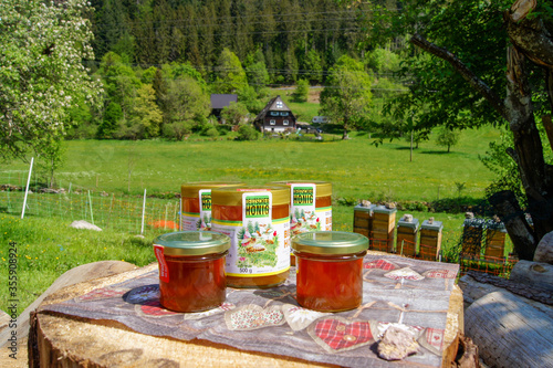 Schonach / Germany - May 17, 2020: Sale of organic forest honey glasses on a table with beehives and a typical German Black Forest house in the background. photo
