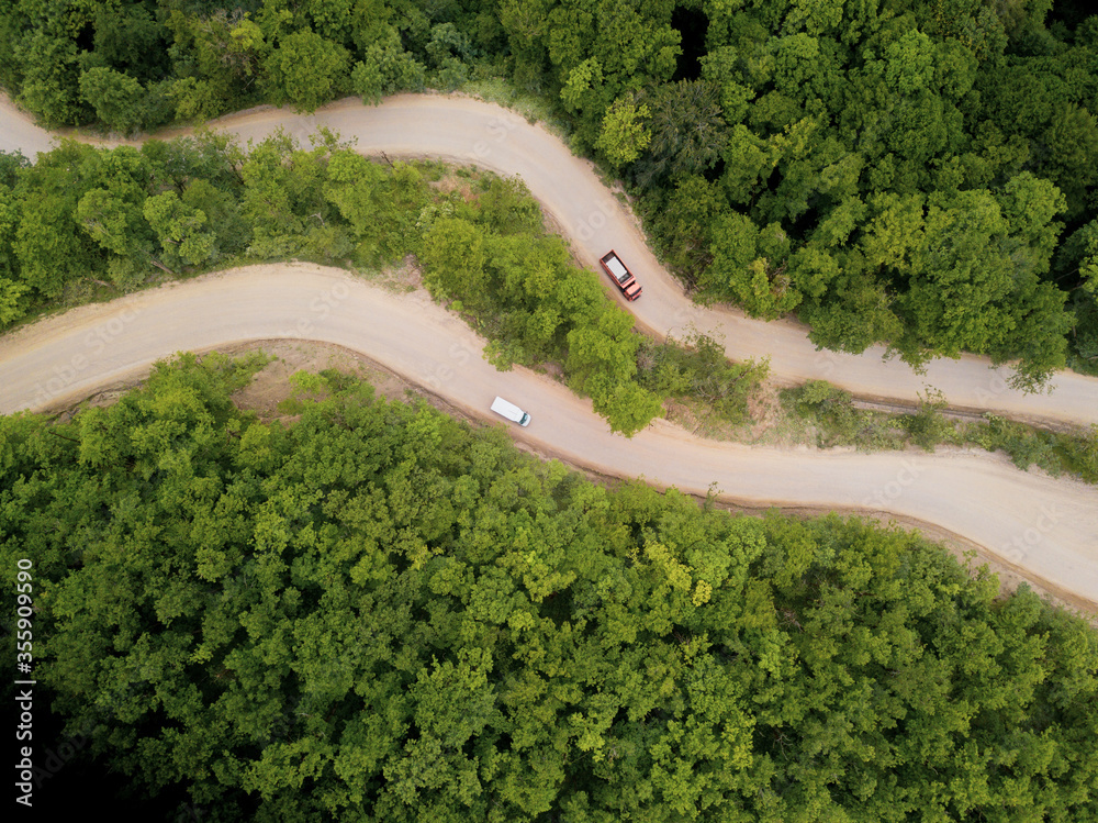 Mountain winding zig zag gravel road. Top aerial view: cars driving on road from above.