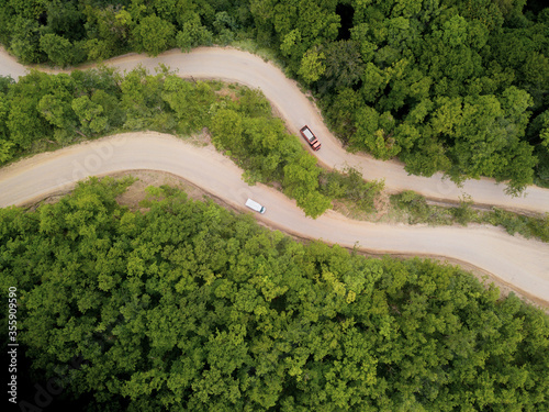 Mountain winding zig zag gravel road. Top aerial view: cars driving on road from above.