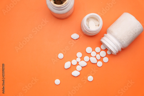 Top view of white pills spilling from container 