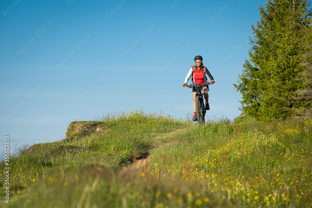 pretty senior woman riding her electric mountain bike on the mountains above Oberstaufen, Allgau Alps, Bavaria Germany 
