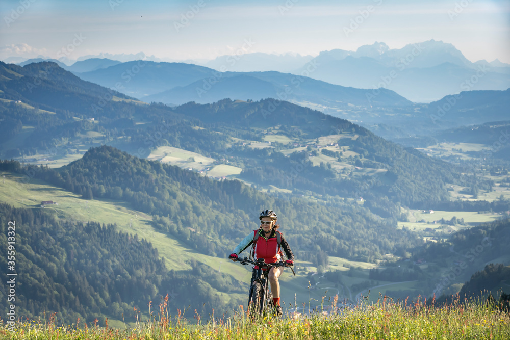 pretty senior woman riding her electric mountain bike on the mountains above Oberstaufen, Allgau Alps, Bavaria Germany 
