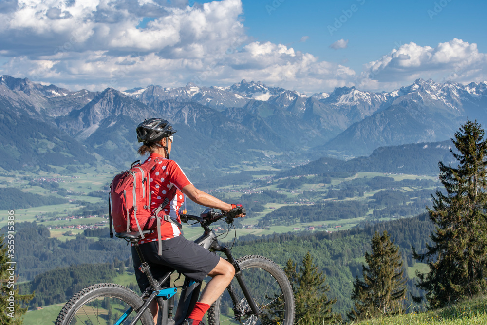 Fototapeta premium pretty senior woman riding her electric mountain bike on the mountains above the Iller valley between Sonthofen and Oberstdorf, Allgau Alps, Bavaria Germany 