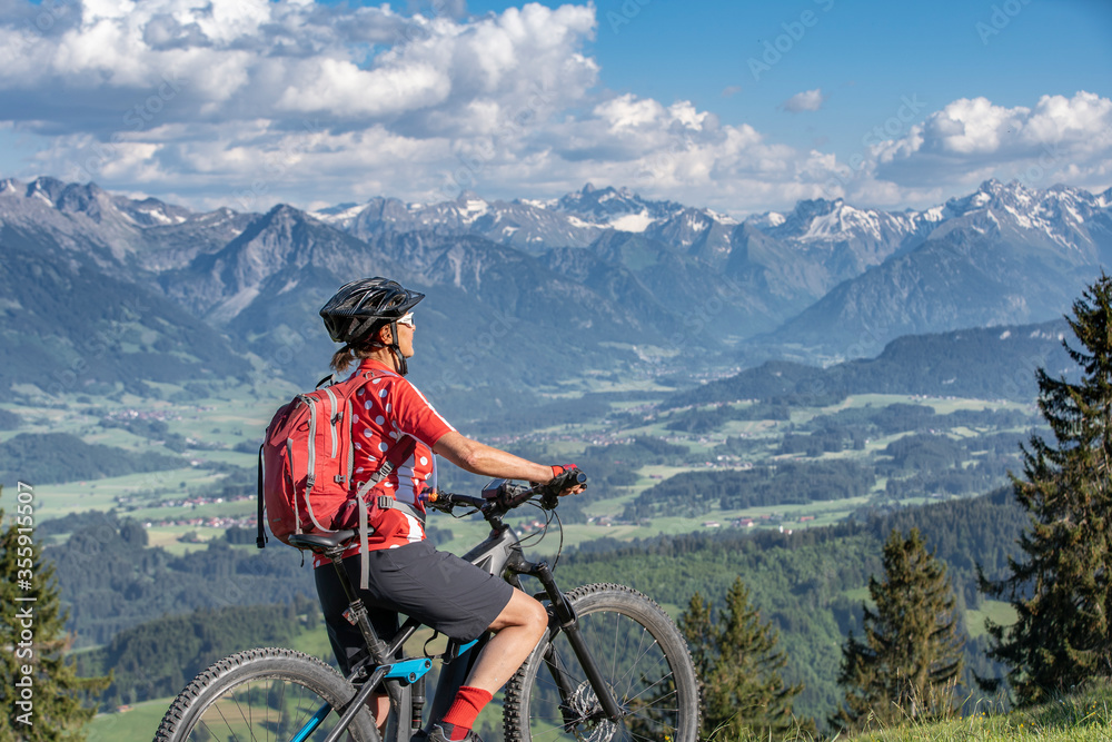 pretty senior woman riding her electric mountain bike on the mountains above the Iller valley between Sonthofen and Oberstdorf, Allgau Alps, Bavaria Germany
