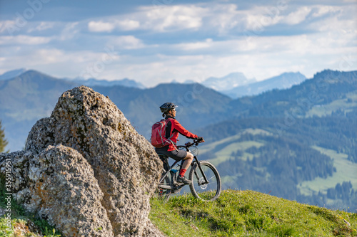 pretty senior woman riding her electric mountain bike in warm dawn sunlight and enjoying the spectacular view over the Allgau alps near Oberstdorf, Bavaria, Germany