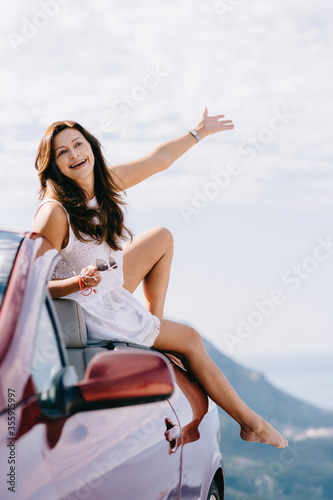 Happy woman sits in a red convertible car with a beautiful view