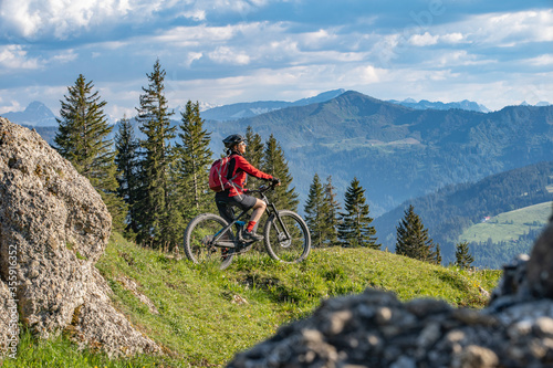 pretty senior woman riding her electric mountain bike in warm dawn sunlight and enjoying the spectacular view over the Allgau alps near Oberstdorf, Bavaria, Germany photo