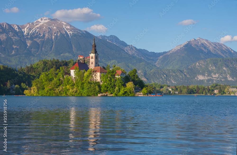 Sunny morning at Lake Bled and Julian Alps in the background. The lake island and charming little church dedicated to the Assumption of Mary are famous tourist attraction in Slovenia
