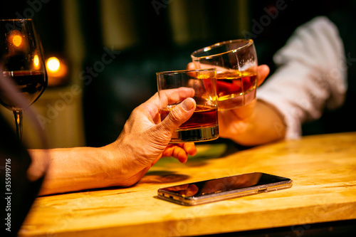 hand holding ice whisky glass  clinking glasses