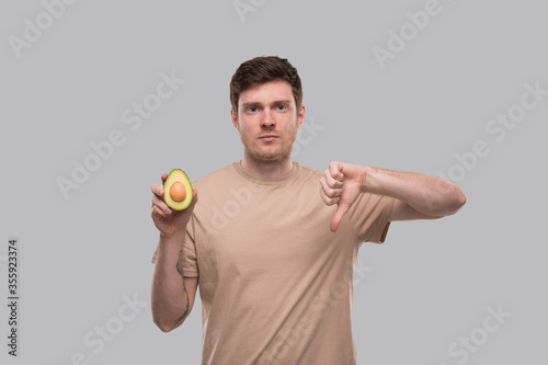 Man Holding Avocado and Thumb Down Close Up Isolated. Avocado Cut in Half. No Avocado, Stop Avocado Concept