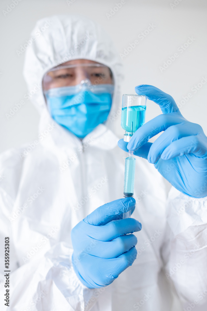 COVID-19 Vaccination concept. Doctor or physician in Personal protective equipment suit (PPE) with mask, goggles and rubber gloves holding syringe and medicine vial for Coronavirus vaccine injection. COVID-19 Vaccination concept. Doctor or physician in Personal protective equipment suit (PPE) with mask, goggles and rubber gloves holding syringe and medicine vial for Coronavirus vaccine injection.