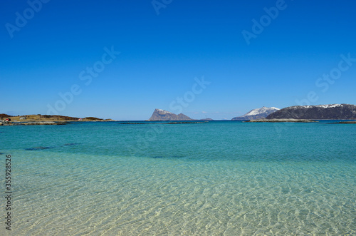majestic white springtime beach with snowy mountain islands in sea on the summer island in northern norway © Arcticphotoworks