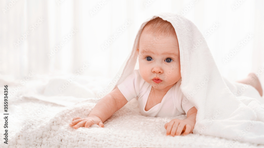 Charming sweet baby is lying on bed under a white blanket on a white background Charming sweet baby is lying on bed under a white blanket on a white background