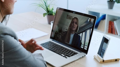 Video of female employee waving and speaking on video call with her colleague on online briefing with laptop at home. photo