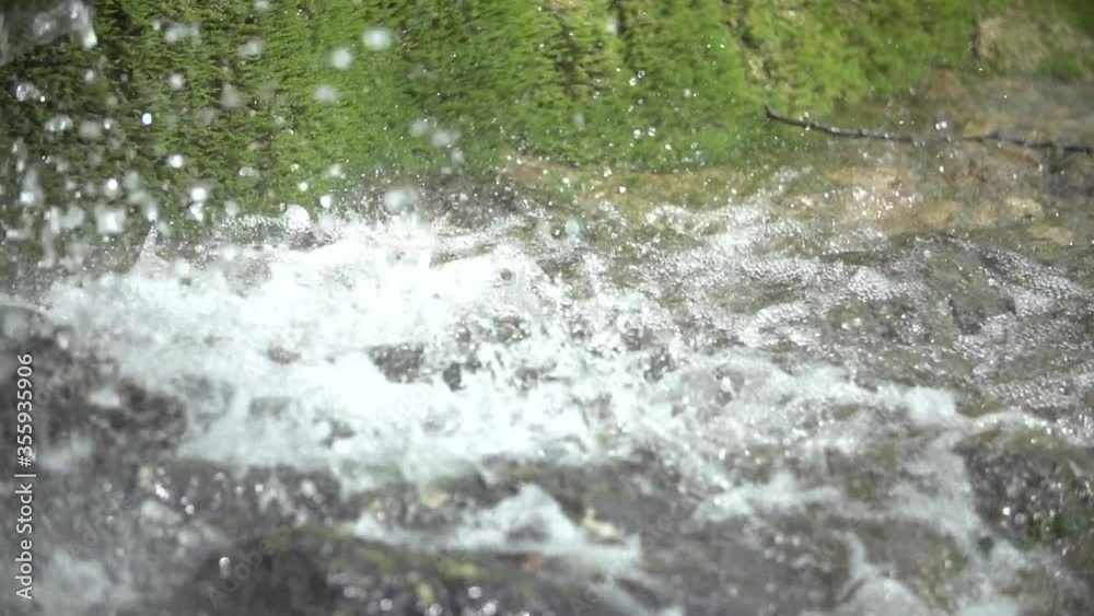 Waterfall drops of water on stone with a stream brook with green moss in the backgound close up slow motion shot Waterfall drops of water on stone with a stream brook with green moss in the backgound close up slow motion shot