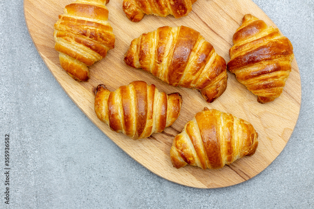 Wooden board with freshly baked croissants on gray background