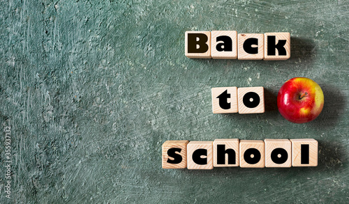 Back to school slogan on wooden cubes. Green blackboard background and ripe apple is a symbol of knowledge. photo