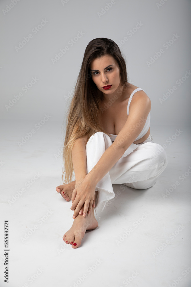 Modelo joven sentada sobre fondo blanco y ropa blanca con pelo largo
