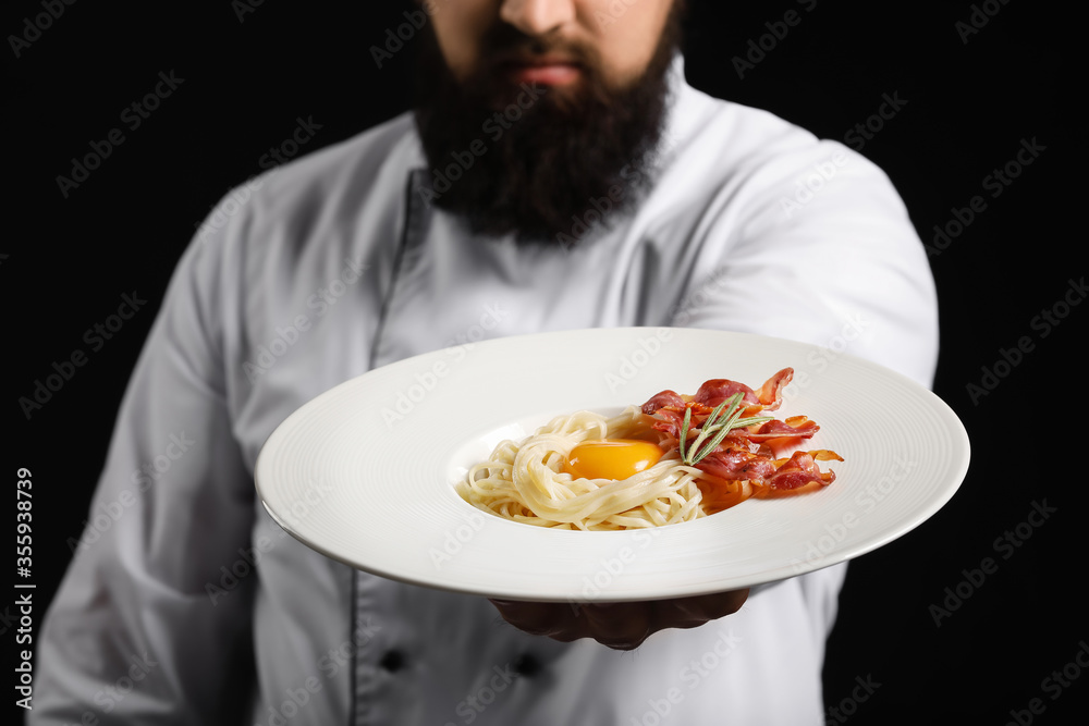 Handsome male chef with tasty pasta carbonara on dark background, closeup Handsome male chef with tasty pasta carbonara on dark background, closeup