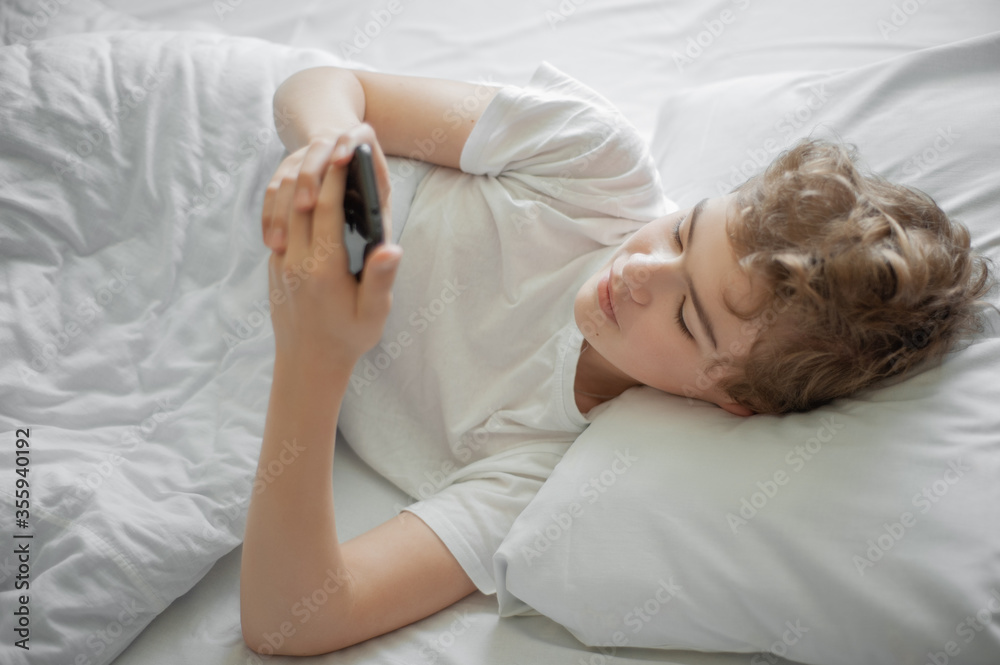 A teenager with a phone lying in bed. A teenager with a phone lying in bed.
