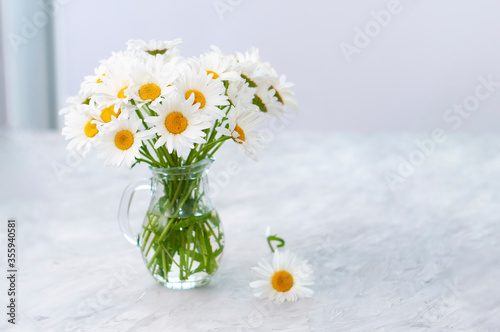 Dried bouquet of white daisies flowers in transparent glass vase on the light gray table in the interior copy space