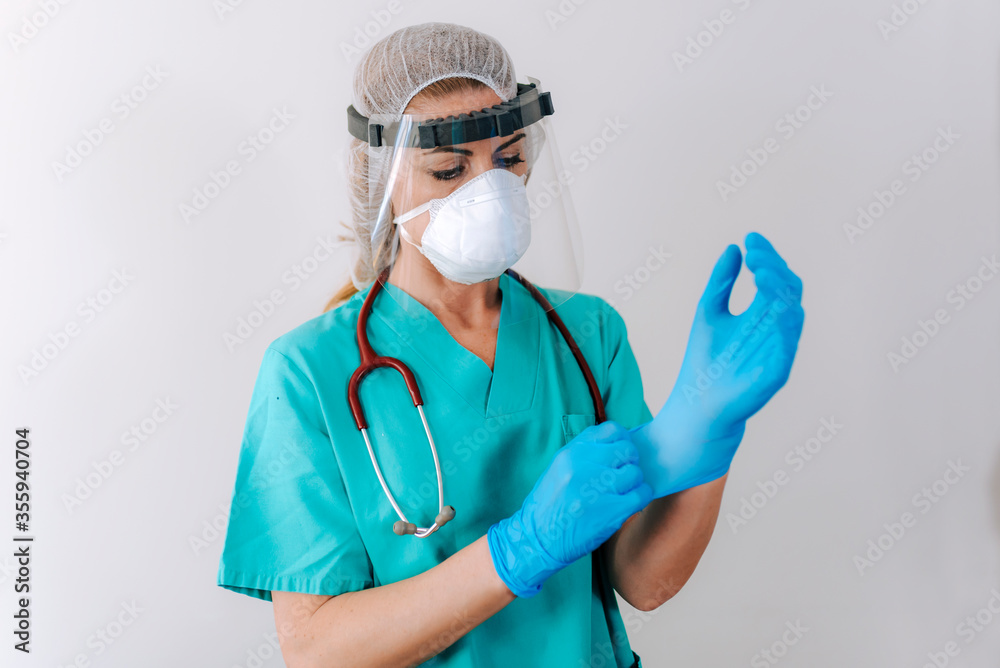 Female young nurse in a medical mask puts on protective surgical sterile gloves on her arm, isolated on gray background, protection against coronovirus. covid-19 protection Female young nurse in a medical mask puts on protective surgical sterile gloves on her arm, isolated on gray background, protection against coronovirus. covid-19 protection