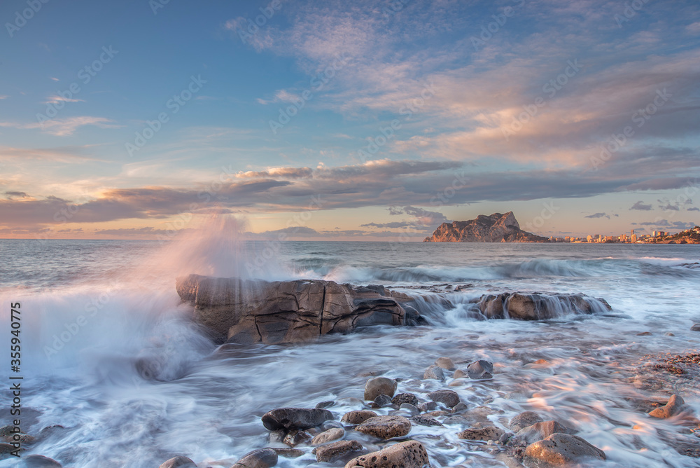Fototapeta premium Paisaje de costa de la cala baladrar, en el mar mediterráneo, atardecer dentro del agua, y el peñón de Ifach de Calpe en el fondo del encuadre.