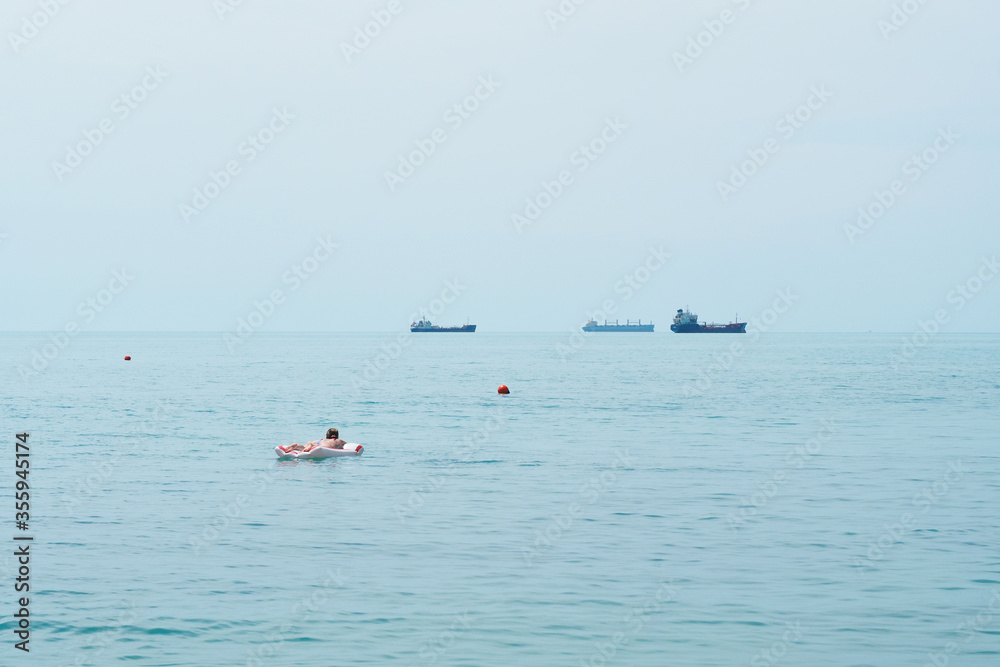 Girl sunbathes on an inflatable raft in the sea, ships in the background, sea horizon