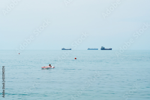 Girl sunbathes on an inflatable raft in the sea, ships in the background, sea horizon