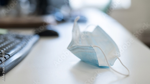 Office employee desktop during a pandemic. Shot of a used mask by the keyboard on a white table. The manager took off the used mask at the workplace. No people.