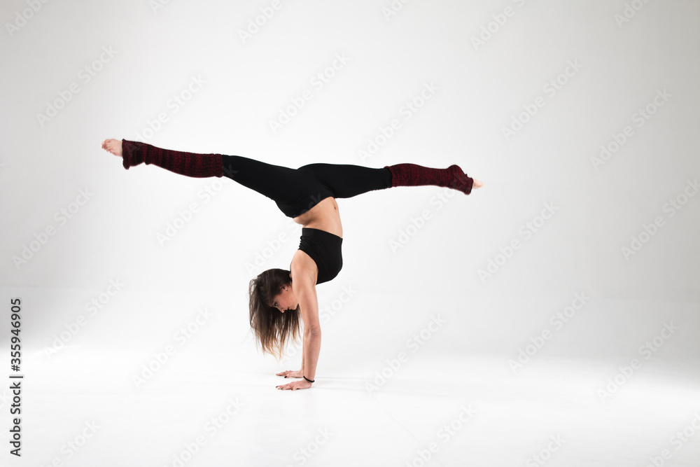 Fototapeta premium Girl in a gymnastic handstand in twine on a white background. Gymnastics, rhythmic gymnastics, practice, workout, strength, flexibility, stretching, performance.