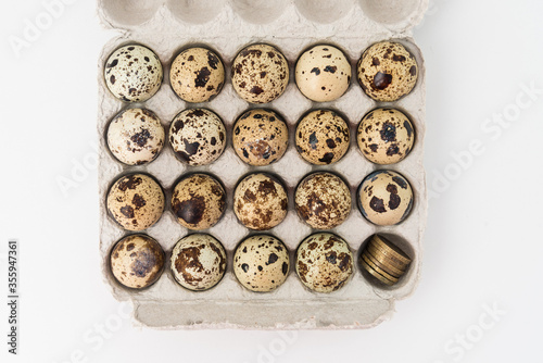 Quail eggs in the egg tray. In one Department, instead of an egg, there are coins. Concept of earnings and expenses in agriculture.