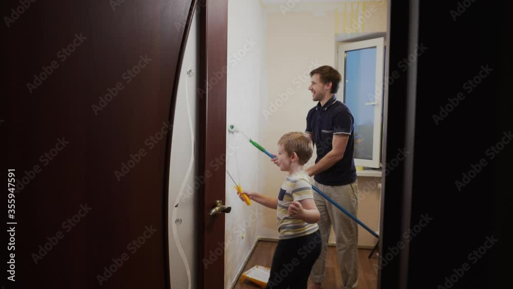 Dad and son cheerfully paint the beige wallpaper on the wall with rollers with white paint, dance, smile Dad and son cheerfully paint the beige wallpaper on the wall with rollers with white paint, dance, smile