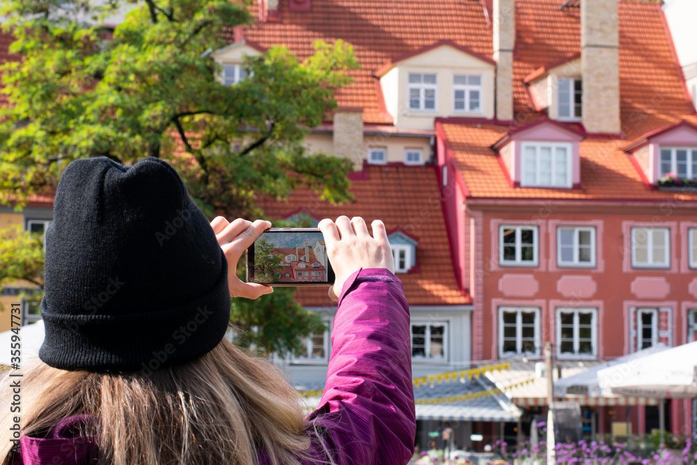 Girl is making photo on her smartphone europian street and houses with orange .tile roof in sunny day, facade of building in art nouveau style.