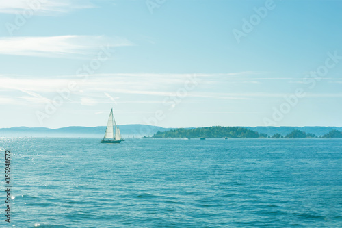 Beautiful seascape with calm blue sea with shiny water surface and sailing boat, vacation on sunny islands. Background with glowing sea and yacht