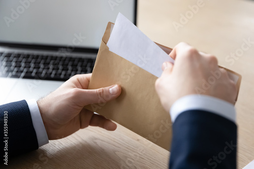 Close up back view of businessman sit at office desk open envelope with postal paper document, male employee unpack post paperwork letter or correspondence with decision notification or law order photo