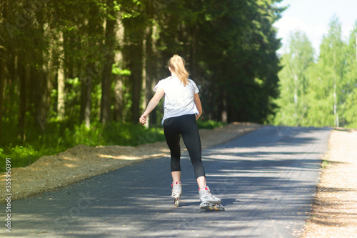 A girl rides roller skates on an asphalt road in the Park in the summer.