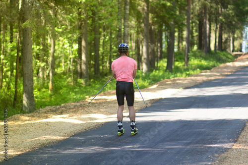A man rides a ski roller on an asphalt road in the Park in the summer.