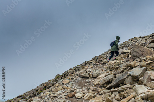 Woman climbing the rocky Scafell Pike against a heavy cloud. This is England s tallest mountain in Cumbria