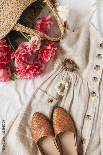 Beauty fashion collage with women's clothes and accessory on white linen. Sun dress sarafan, leather shoes, pink peony flowers in straw bag. Flat lay, top view fashion blog lifestyle concept
