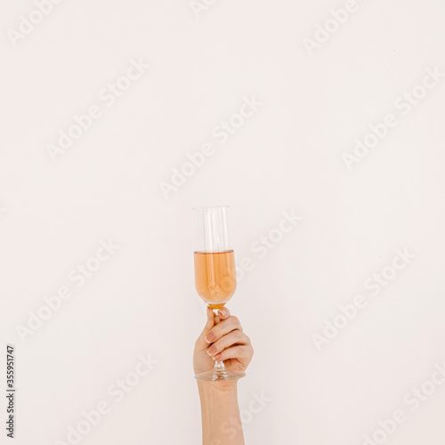 Cheers! Women's hand holding glass of rose champagne against white wall. Happy Birthday, anniversary party celebrating decoration festive concept
